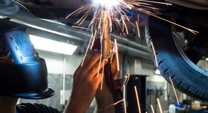 A metal fabricator repairing the bottom of a vehicle using a welder