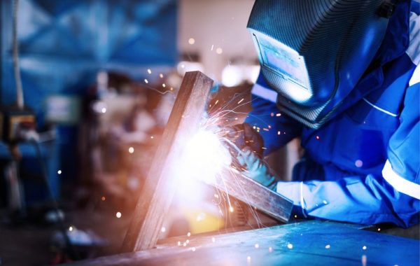 A welder performing on-site metal repair for an industrial facility's machinery